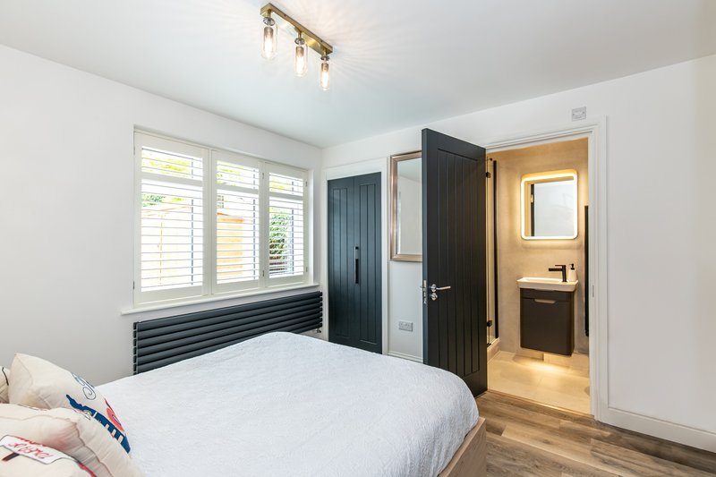 Modern bedroom with double bed, white shuttered windows, black wardrobe and ensuite bathroom visible