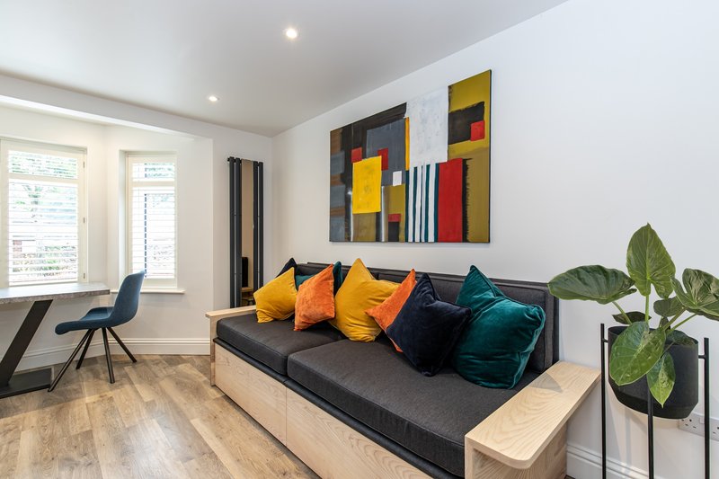 Modern living room with black sofa, colorful cushions, abstract wall art, and potted plant