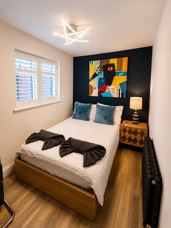 Compact bedroom with wooden bed, white bedding, black accent wall, colourful abstract art, and window with shutters