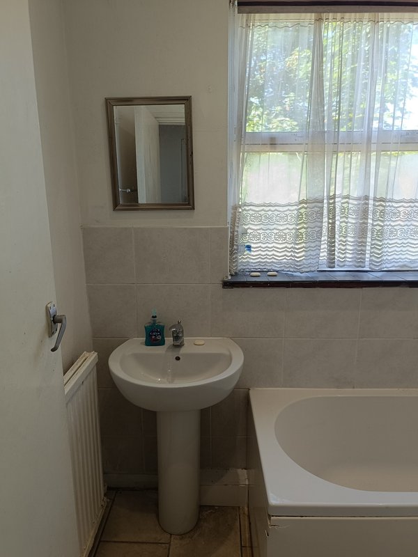 Bathroom with pedestal sink, mirror, bathtub and window with lace curtains