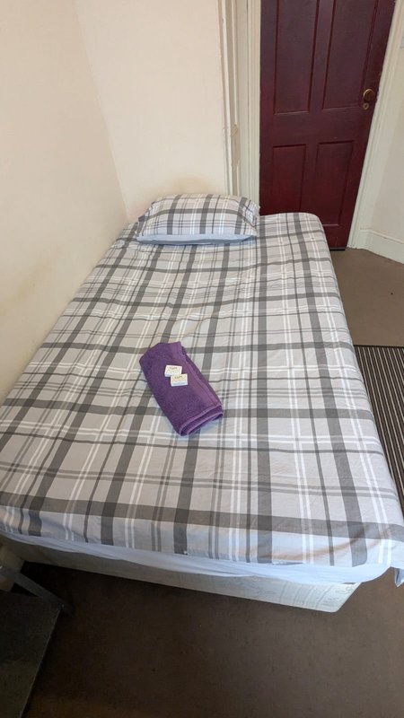 Single bed with checkered bedding, pillow, and purple cushion in bedroom