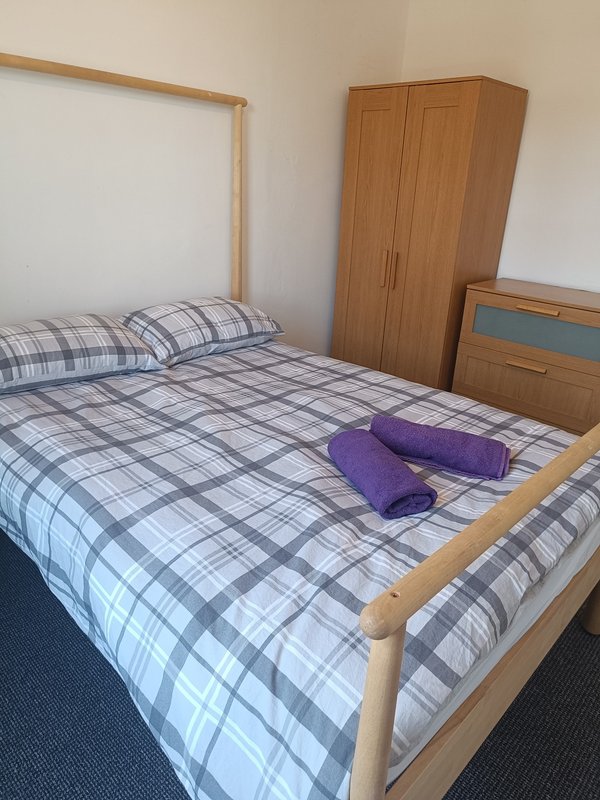 Bedroom with wooden bed, plaid bedding, purple towels, wardrobe and dresser