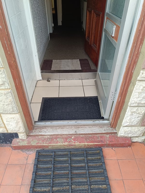 Entryway and narrow hallway with tiled floor, dark doormats and red-painted door frame