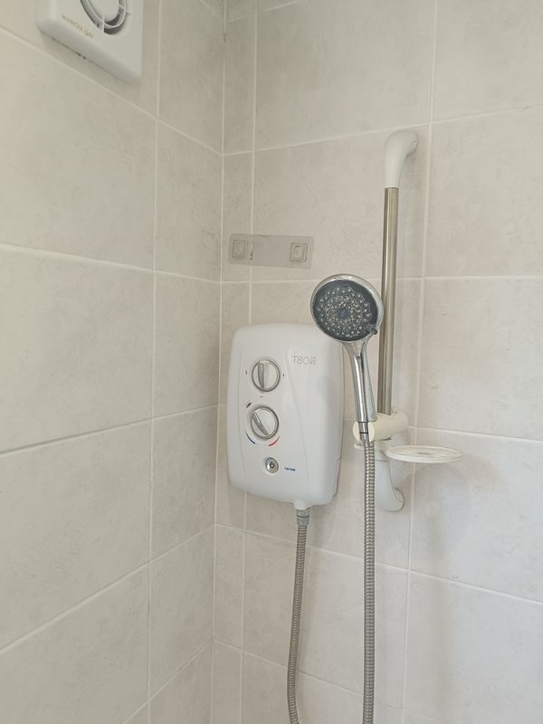 Bathroom shower area with electric heater unit, handheld showerhead and tiled walls