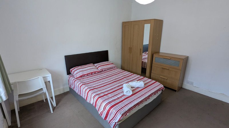Bedroom with double bed, striped bedding, wooden wardrobe, white desk and dark flooring.