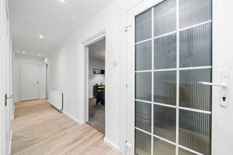 Modern hallway with wooden flooring, white walls, glass partition doors and recessed lighting