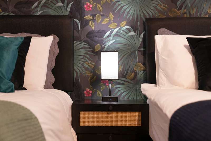 Twin bedroom with dark headboard, tropical wallpaper, white bedding and decorative cushions