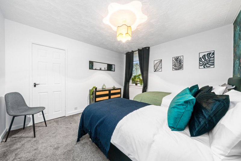 Modern bedroom with double bed, teal and navy bedding, gray chair, and wall art