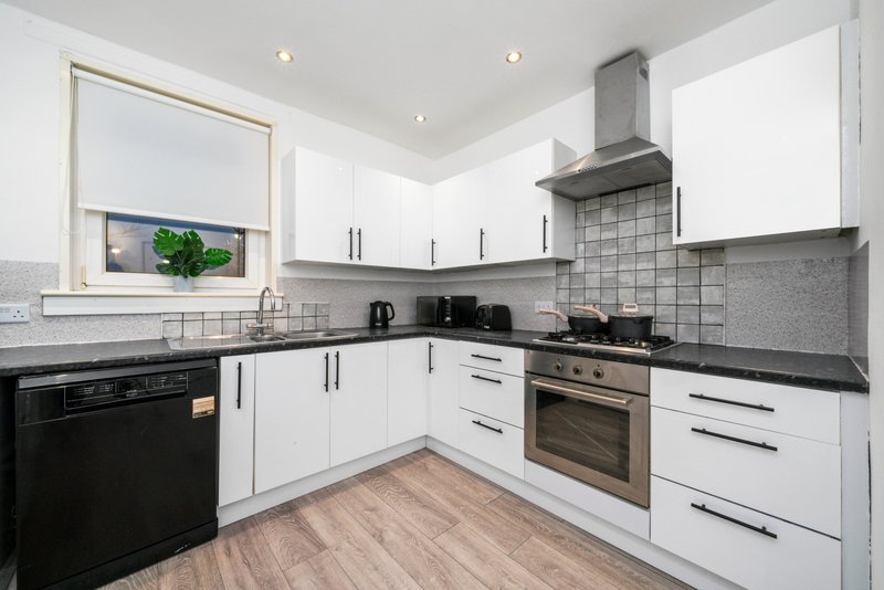 Modern kitchen with white cabinetry, black appliances, gray tile backsplash and wooden flooring