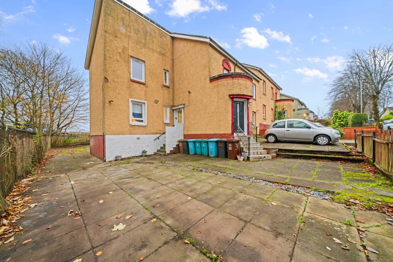 Exterior view of brick house with paved driveway, parked car, and garden fencing