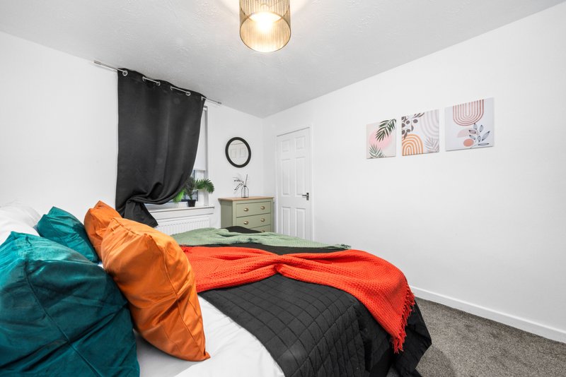 Bedroom with colorful bedding, pendant light, dresser, and wall art