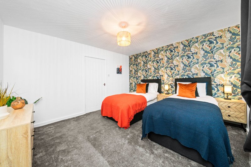 Bright bedroom with two single beds, patterned wallpaper, wooden furniture and ceiling light