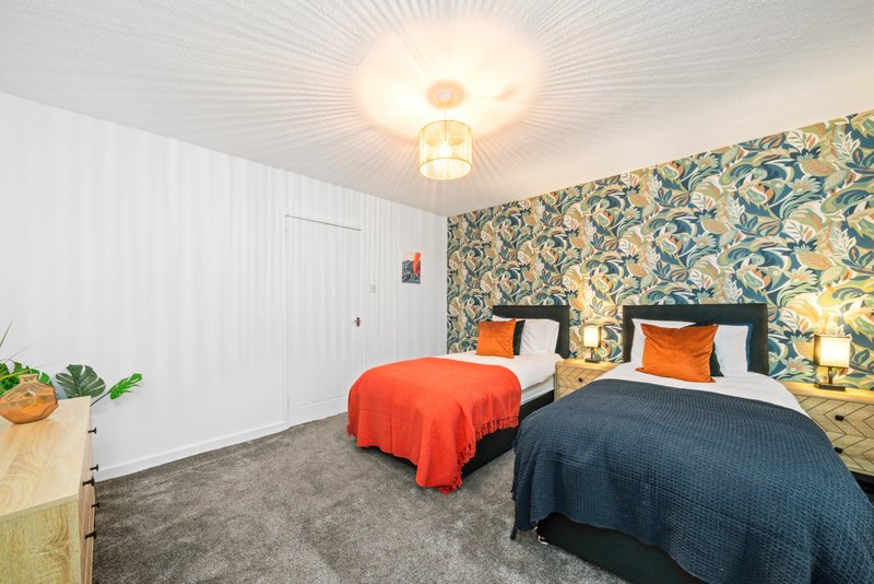 Bright bedroom with two beds, patterned wallpaper, potted plant and ceiling light
