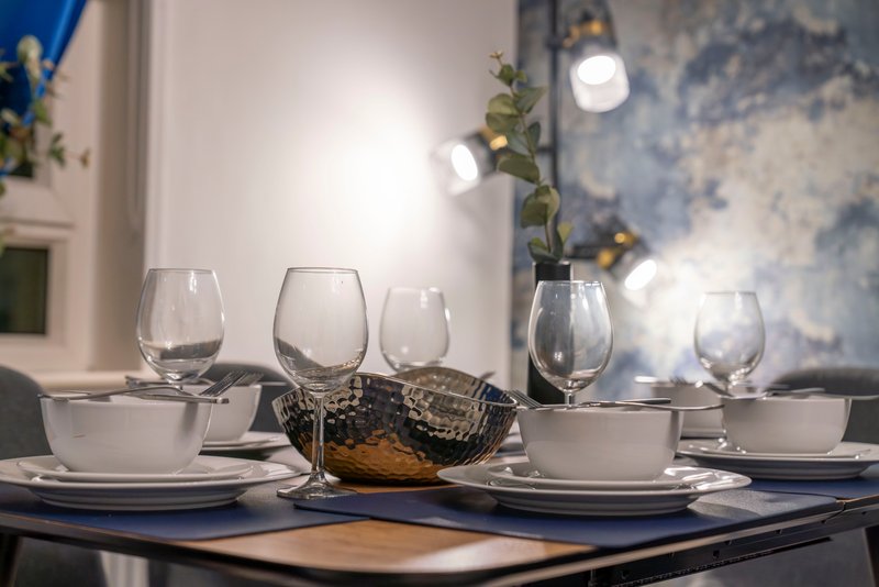 Dining table set with white plates, glasses, bowls and decorative centerpiece under pendant lighting