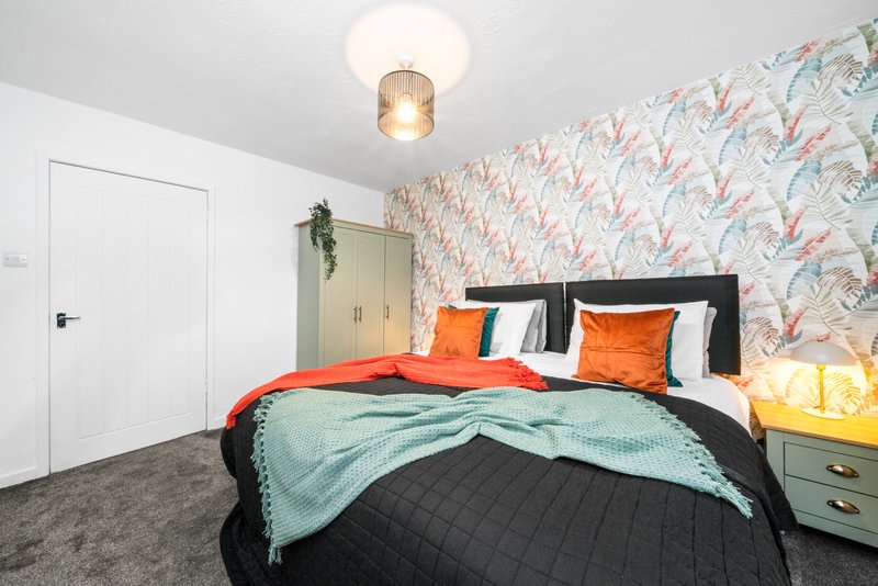 Bedroom with double bed, orange pillows, patterned wallpaper, ceiling light, and white door