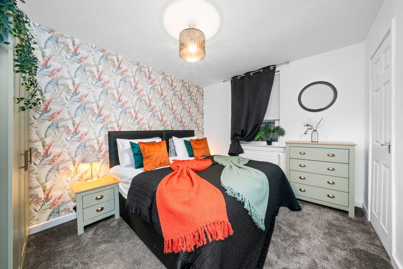 Bedroom with patterned feature wall, double bed with colorful pillows, wooden dresser and pendant light