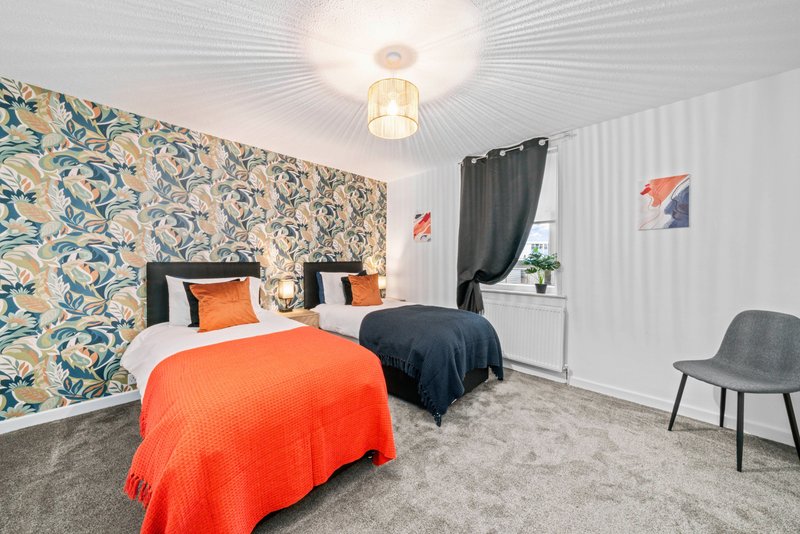 Twin bedroom with patterned feature wall, orange bedding, grey carpet and ceiling light