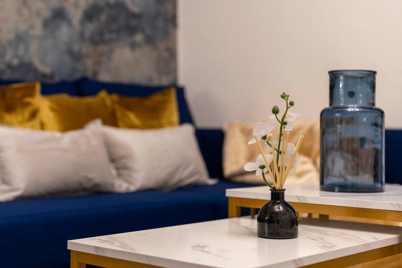 Living room with blue sofa, yellow cushions, marble table, dried flowers in vase