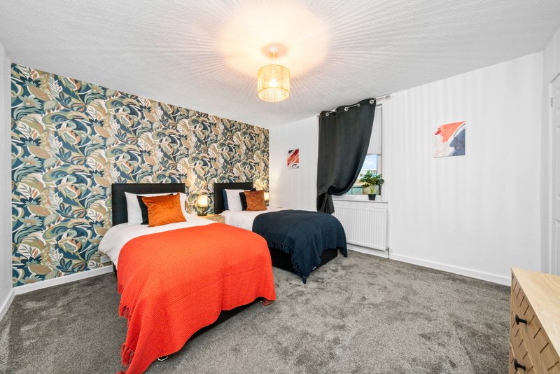 Bedroom with two single beds, patterned feature wall, ceiling light and window with black curtain