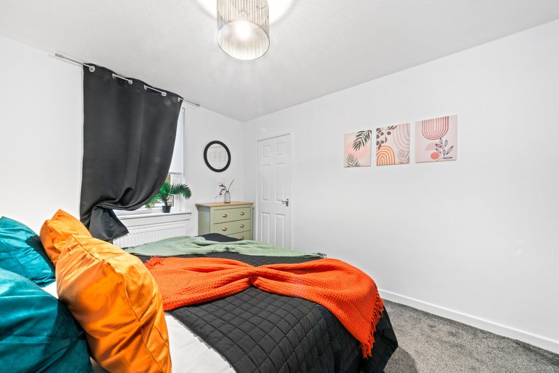 Bedroom with double bed, colorful bedding, black curtain, dresser and wall art