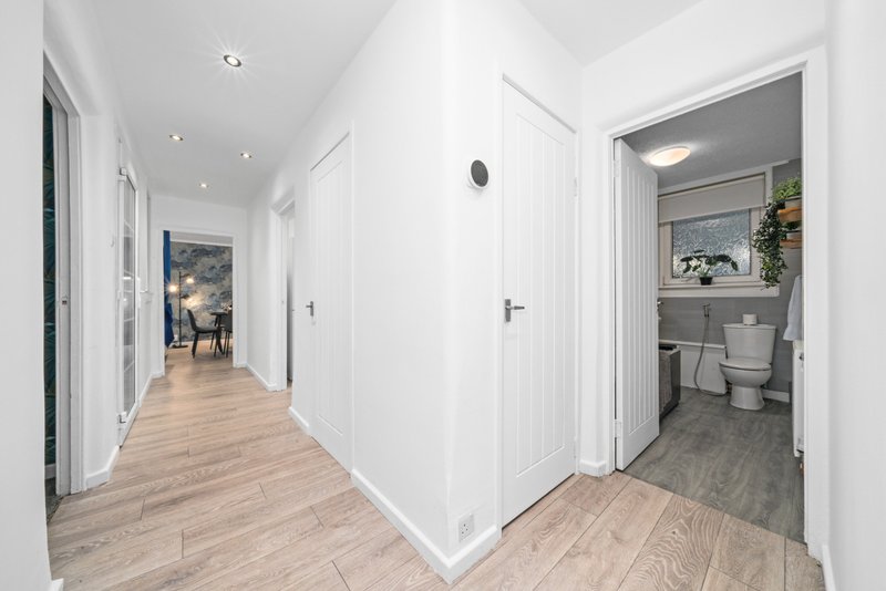 Bright hallway with wooden flooring, white doors, and bathroom entrance visible on right