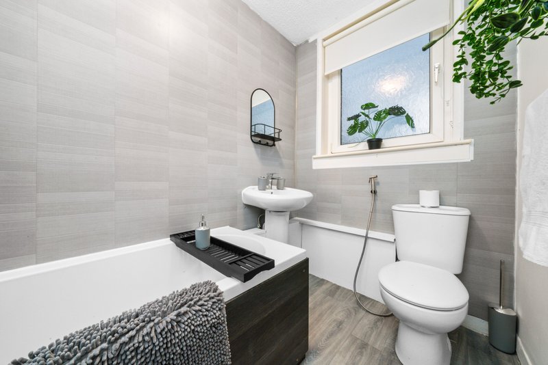Modern bathroom with bathtub, pedestal sink, toilet, and window with plants