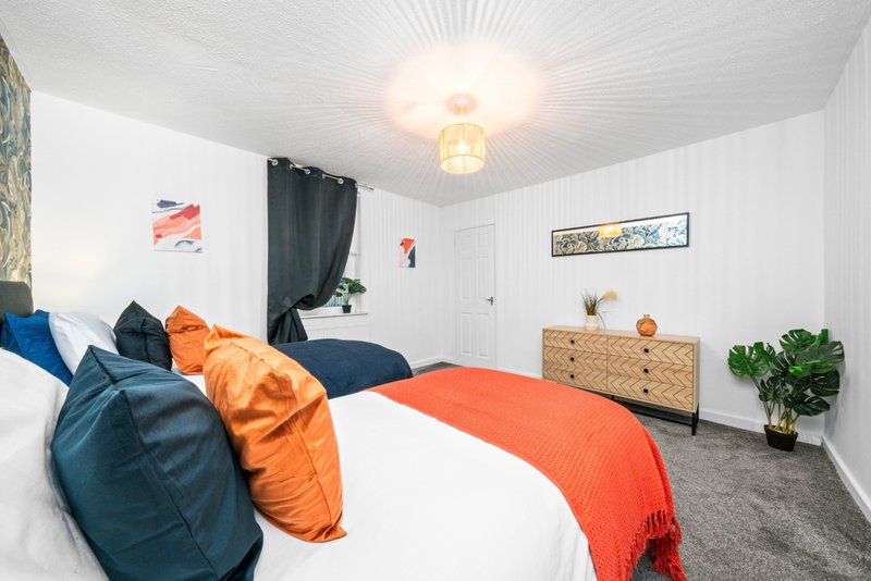 Bright bedroom with double bed, orange and blue pillows, wooden dresser, and potted plant
