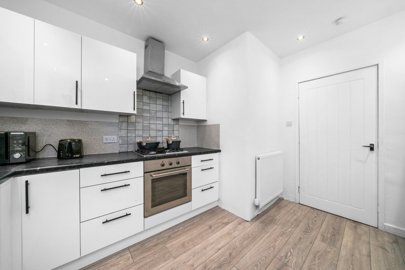 Modern kitchen with white cabinetry, gray tile backsplash, built-in oven and wooden flooring