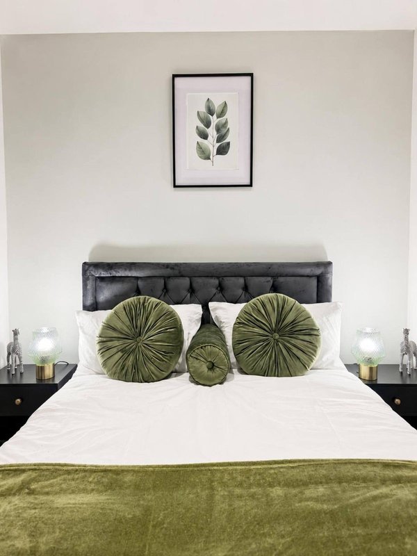 Bedroom with grey upholstered headboard, white bedding, green cushions and throw, framed botanical print above bed