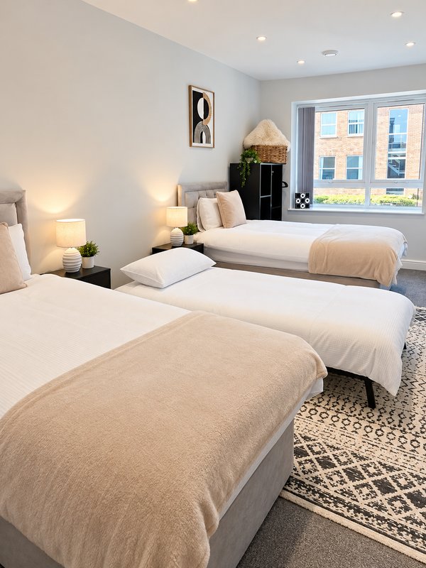Modern twin bedroom with two single beds, bedside lamps, neutral décor and large windows with city view