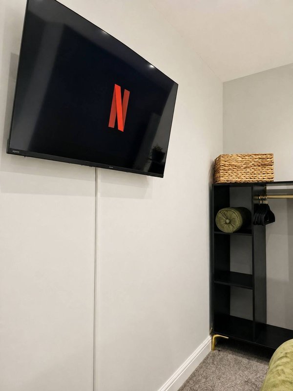 Bedroom corner with wall-mounted television, black shelving unit, and woven basket decor