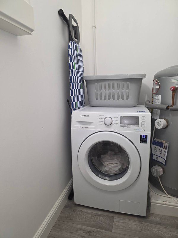 Utility room with white washing machine, laundry basket, and wall-mounted drying rack