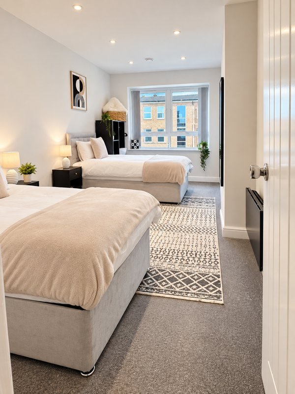 Twin bedroom with two beds, lamps, plants and garden view through patio doors