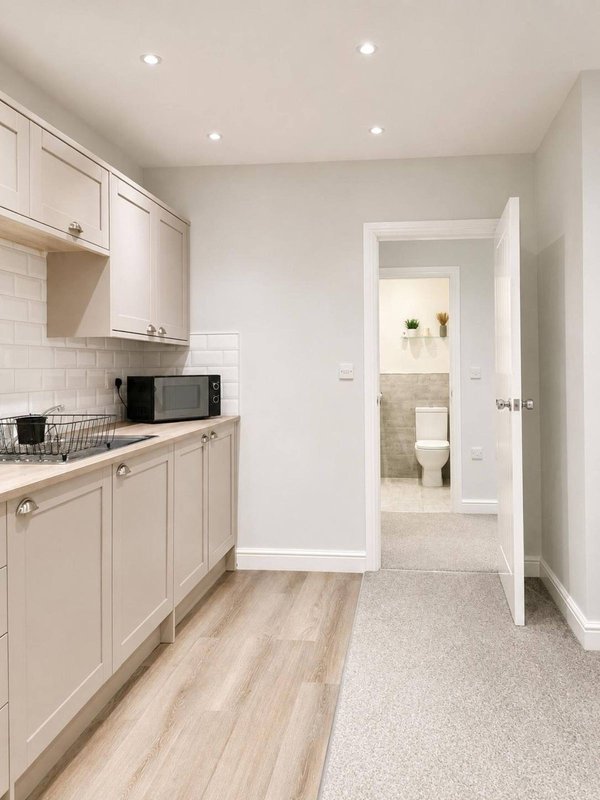 Modern kitchen with cream cabinetry, subway tile splashback, wooden flooring and open doorway to bathroom