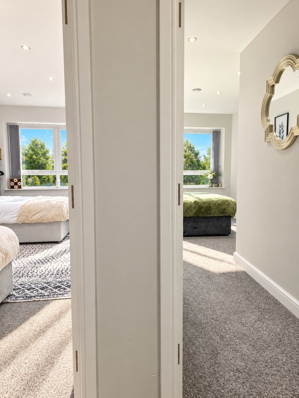 Hallway with open door to bedroom, natural light from windows, grey carpet and white walls