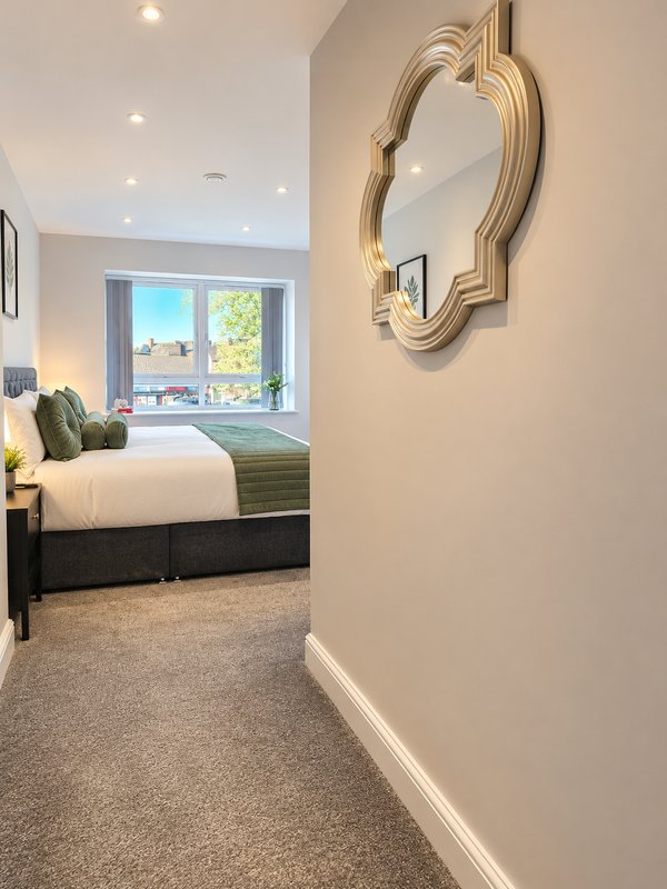 Hallway with decorative mirror leading to bedroom with double bed and window