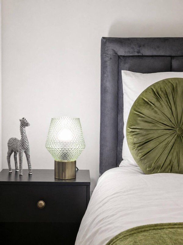 Modern bedroom with dark upholstered headboard, white bedding, green cushion, and black nightstand with decorative lamp