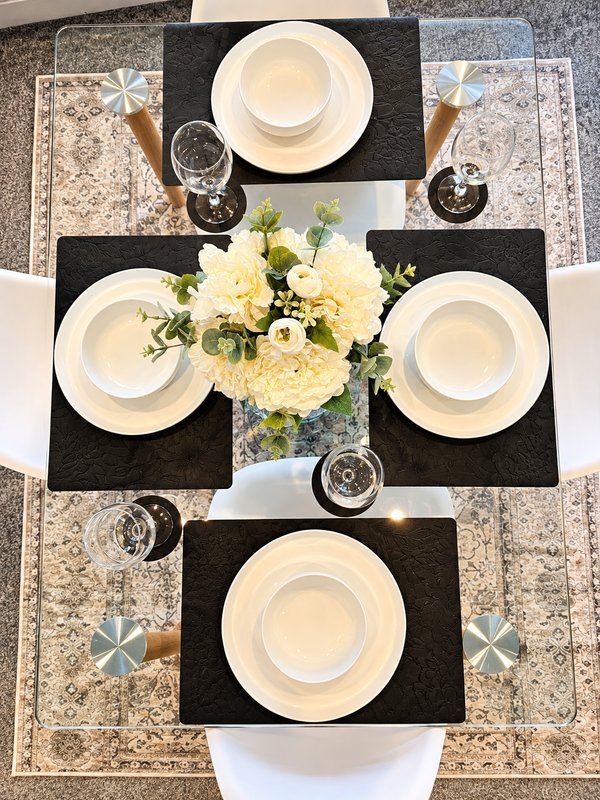 Overhead view of formal dining table with four place settings, white plates, and yellow floral centerpiece