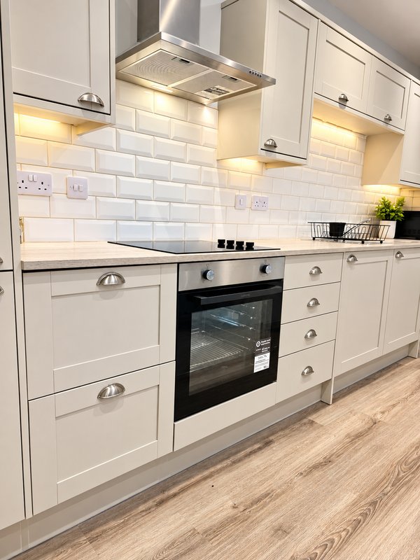 Modern kitchen with white cabinetry, integrated oven, range hood, subway tile backsplash and wooden flooring