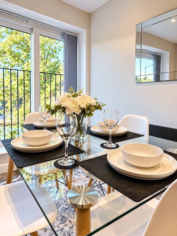 Dining room with black glass table, place settings, flowers, and glass doors overlooking garden
