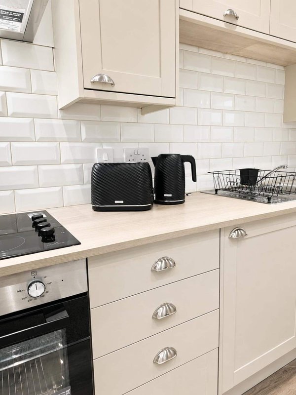 Modern cream kitchen with white subway tile backsplash, black appliances, and countertop toaster and kettle