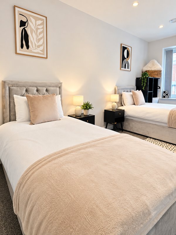 Modern bedroom with twin beds, neutral bedding, bedside lamps, and framed wall art