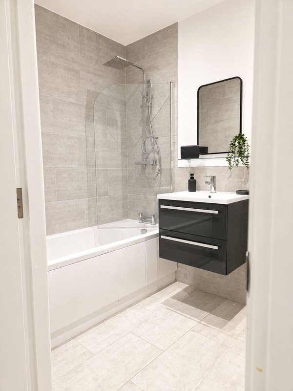 Modern bathroom with walk-in shower, white bathtub, black vanity unit and mirror