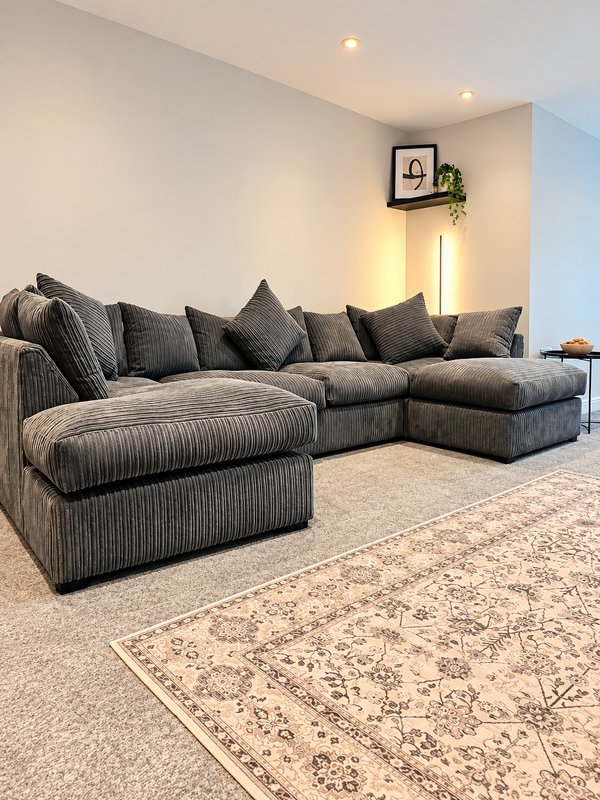 Modern living room with large grey corner sofa, patterned area rug, and wall-mounted clock