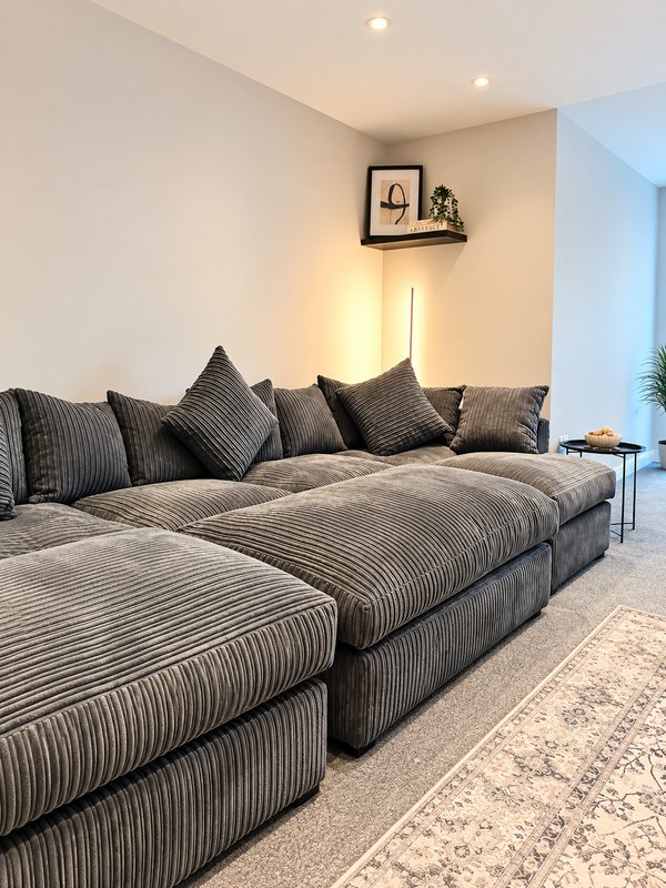 Modern living room with large gray striped sectional sofa, decorative cushions, wall art, and recessed lighting