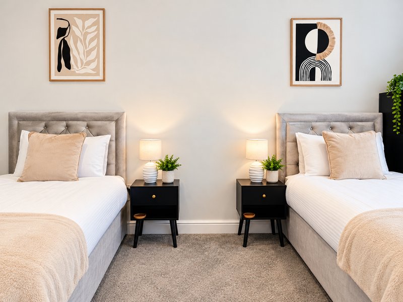 Twin bedroom with two single beds, nightstands, lamps, and framed wall art