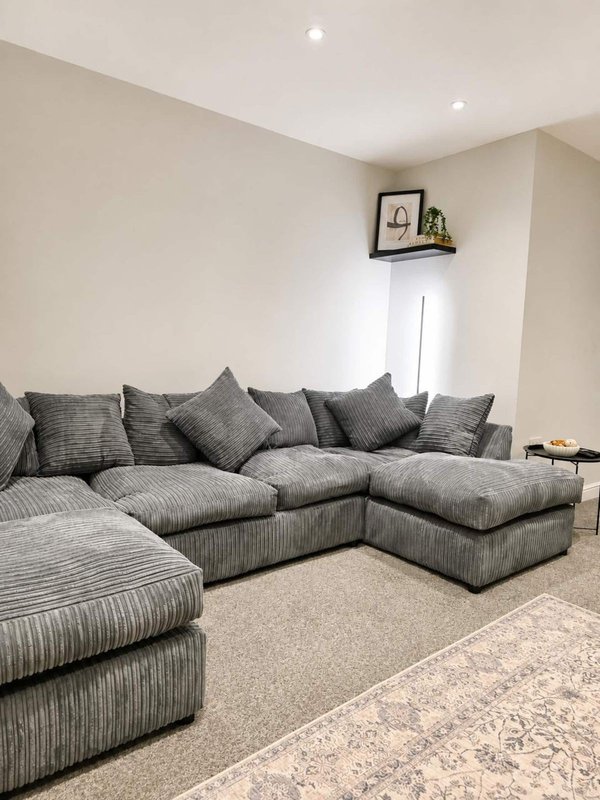 Modern living room with large grey corner sofa, multiple cushions, and beige carpet flooring