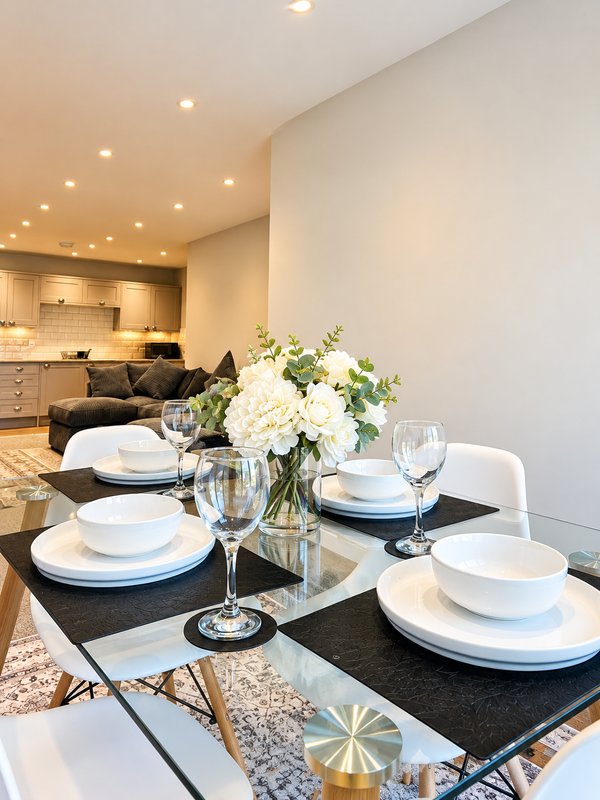 Dining table set with white plates and glasses, kitchen visible in background