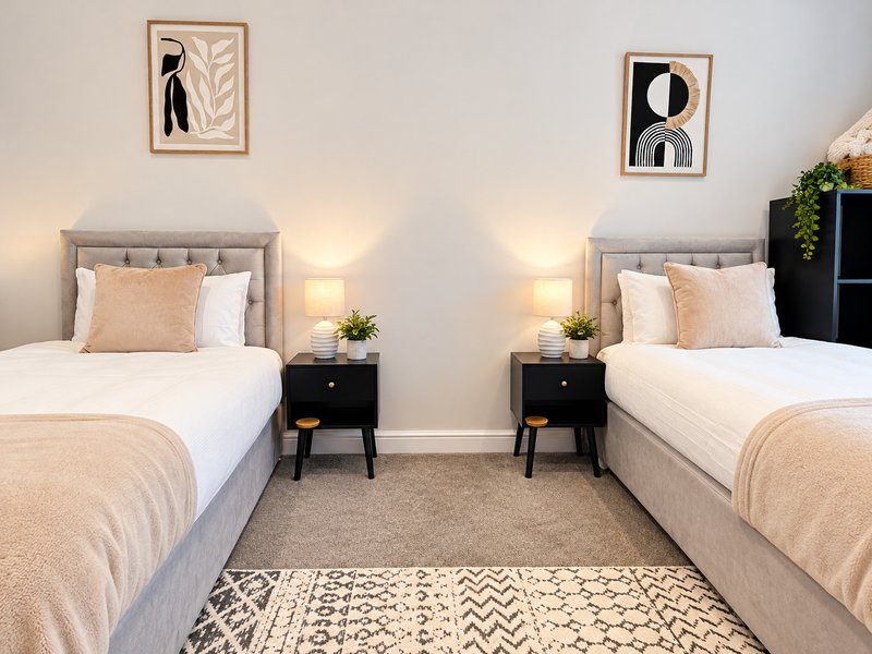 Shared bedroom with two single beds, grey headboards, bedside tables, wall art, and neutral décor