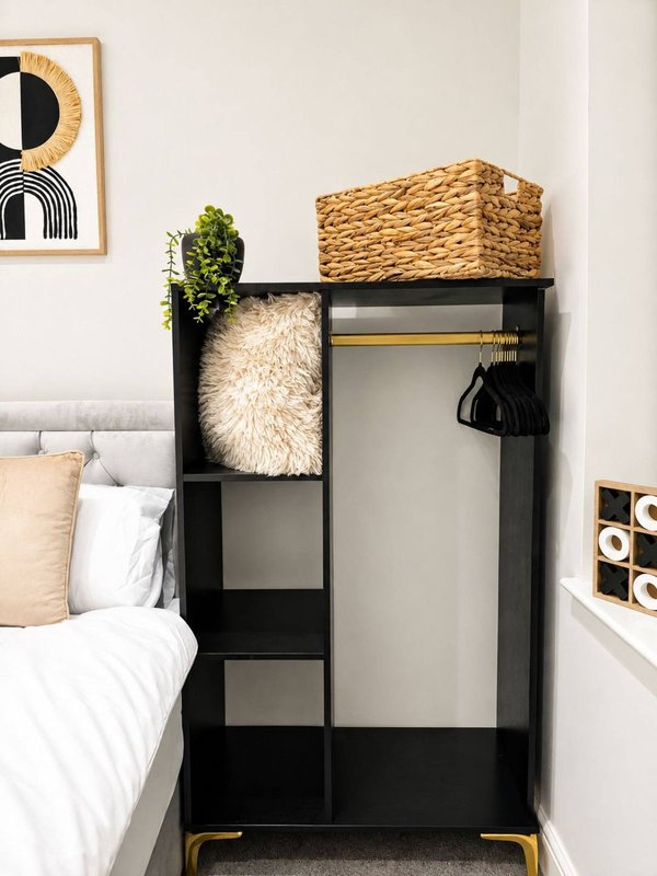 Bedroom corner with black shelving unit, woven storage basket, sheepskin throw, and framed abstract wall art